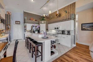 Eine moderne Küche mit weißen Schränken, einer zentralen Kochinsel mit Barhocker und einem Essbereich mit Holztisch und Stühlen.
