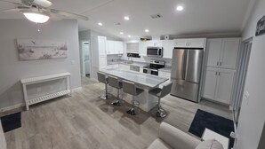 Une cuisine moderne avec des meubles blancs, des appareils en acier inoxydable et un îlot central doté de tabourets de bar.