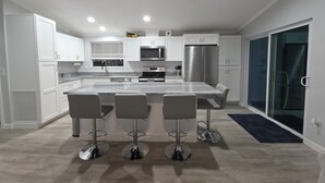 Une cuisine moderne avec des meubles blancs, des appareils en acier inoxydable et un îlot central doté de tabourets de bar.