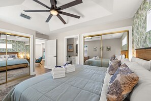 A modern bedroom with a large bed, a ceiling fan, and a bathroom visible through an open door. - Paradise Palms! Quiet West End PCB Retreat! Walk to Beach! Sleeps 8! (Panama City Beach)