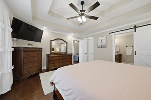 Ein Schlafzimmer mit Bett, Schminktisch, Spiegel, Deckenventilator, Fernseher und Schiebetüren.
