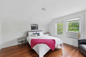Une chambre à coucher comprenant un lit, une table de chevet, une chaise, une fenêtre donnant sur des arbres et un luminaire au plafond.