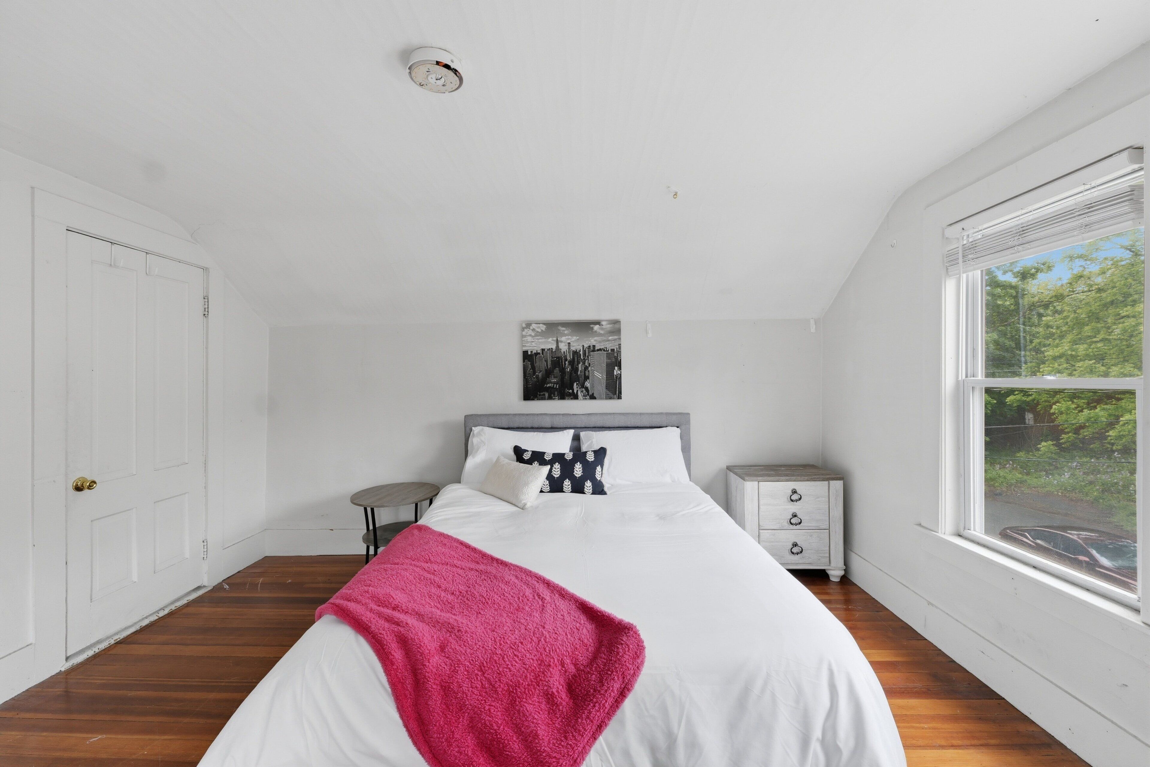 A bedroom with a bed, a nightstand, a window, and a door.