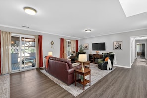 A living room with a brown leather sofa, a green armchair, a wooden coffee table, a flat-screen TV, and a sliding glass door leading to an outdoor patio. - World Cup 2026 Retreat In The Heart Of Montclair 3 Bedroom Condo (Montclair)