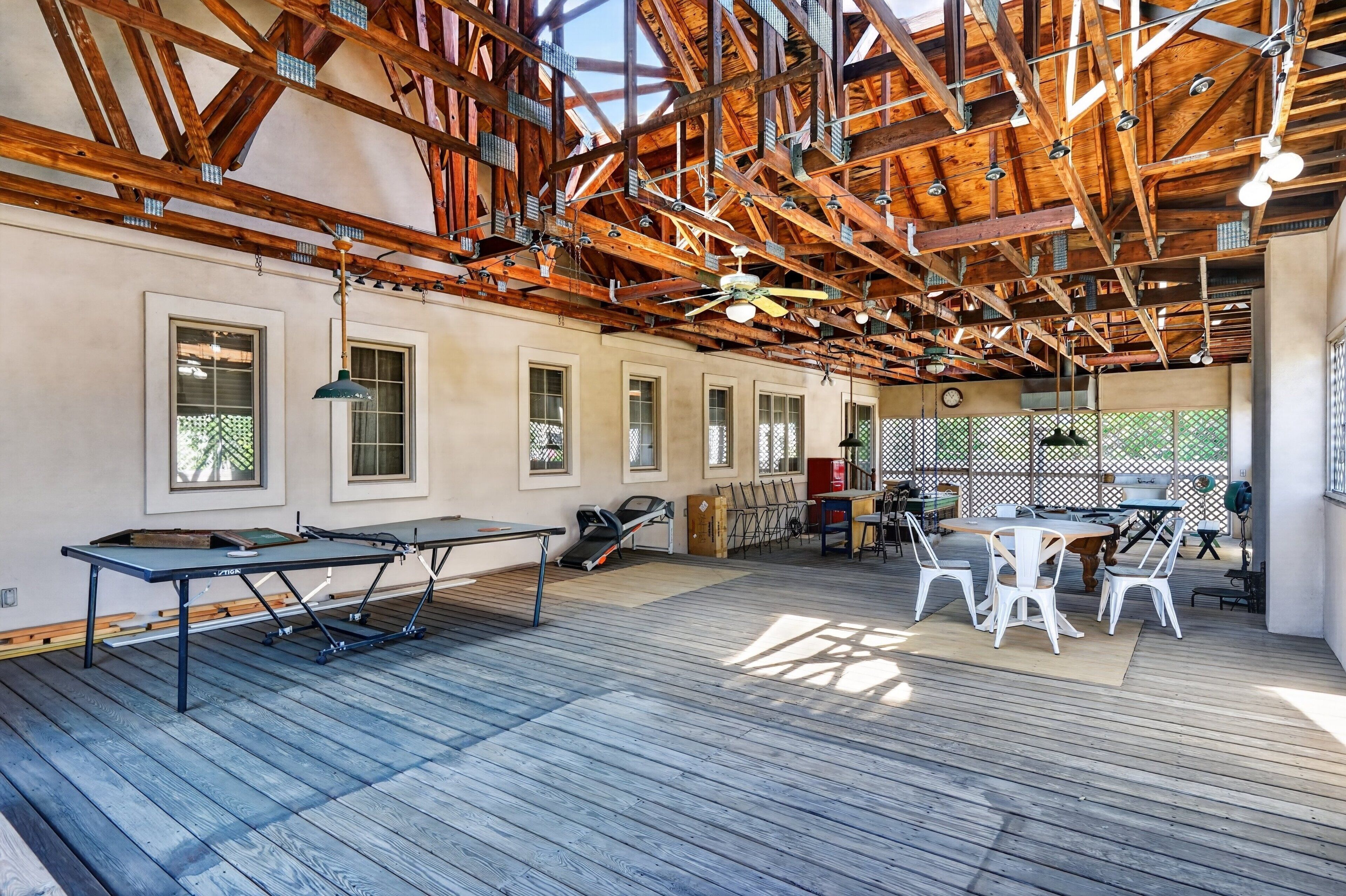 An indoor space with a wooden ceiling, ping pong tables, and a seating area with chairs and a table.