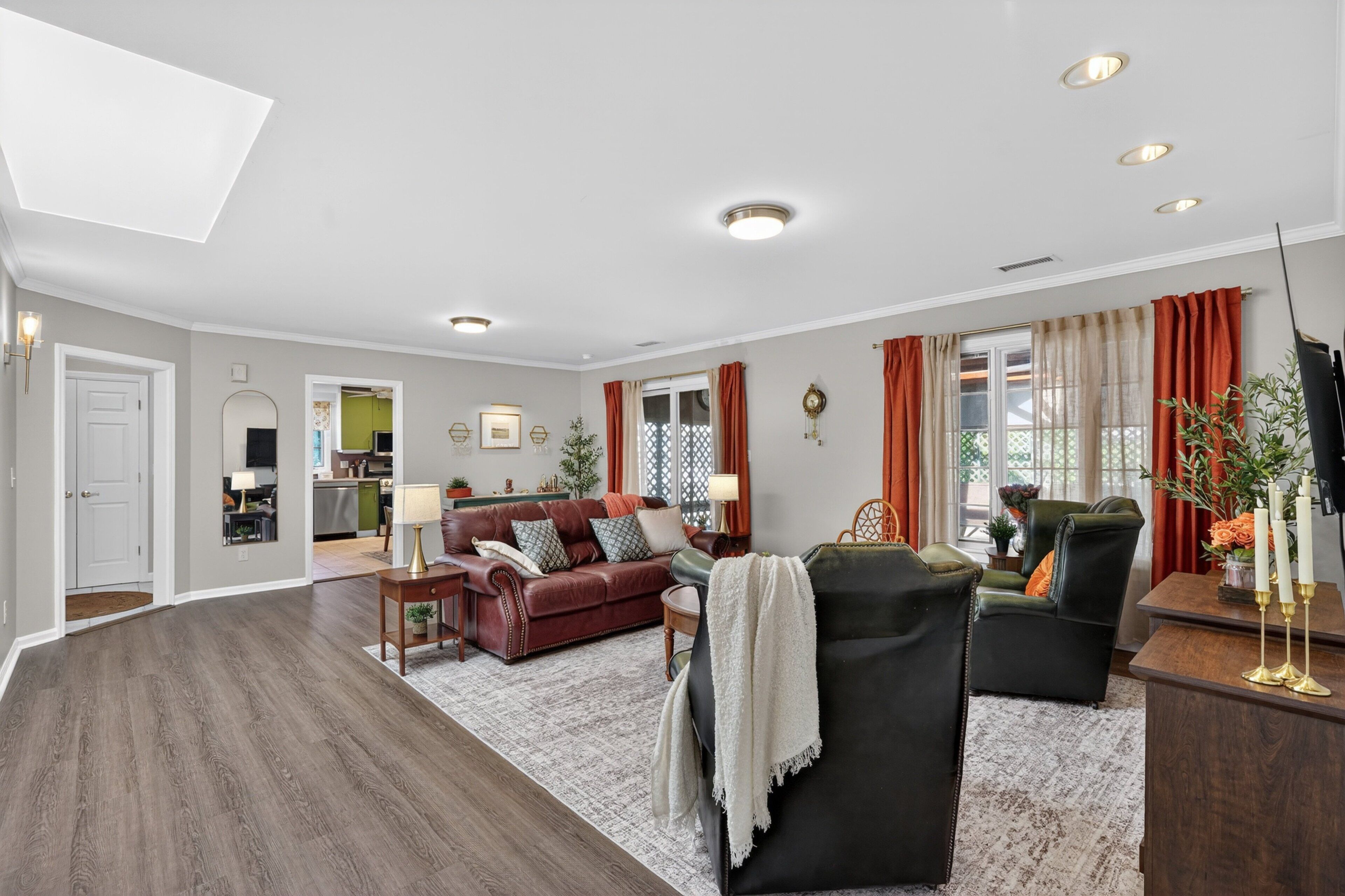 A spacious living room with a dark wood floor, a red leather sofa, a black armchair, and a dining area with a wooden table and chairs.