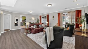 Un salón espacioso con piso de madera oscura, un sofá de cuero rojo, un sillón negro y una zona de comedor con una mesa y sillas de madera.