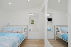 A bedroom with two beds, a window, and a mirror.