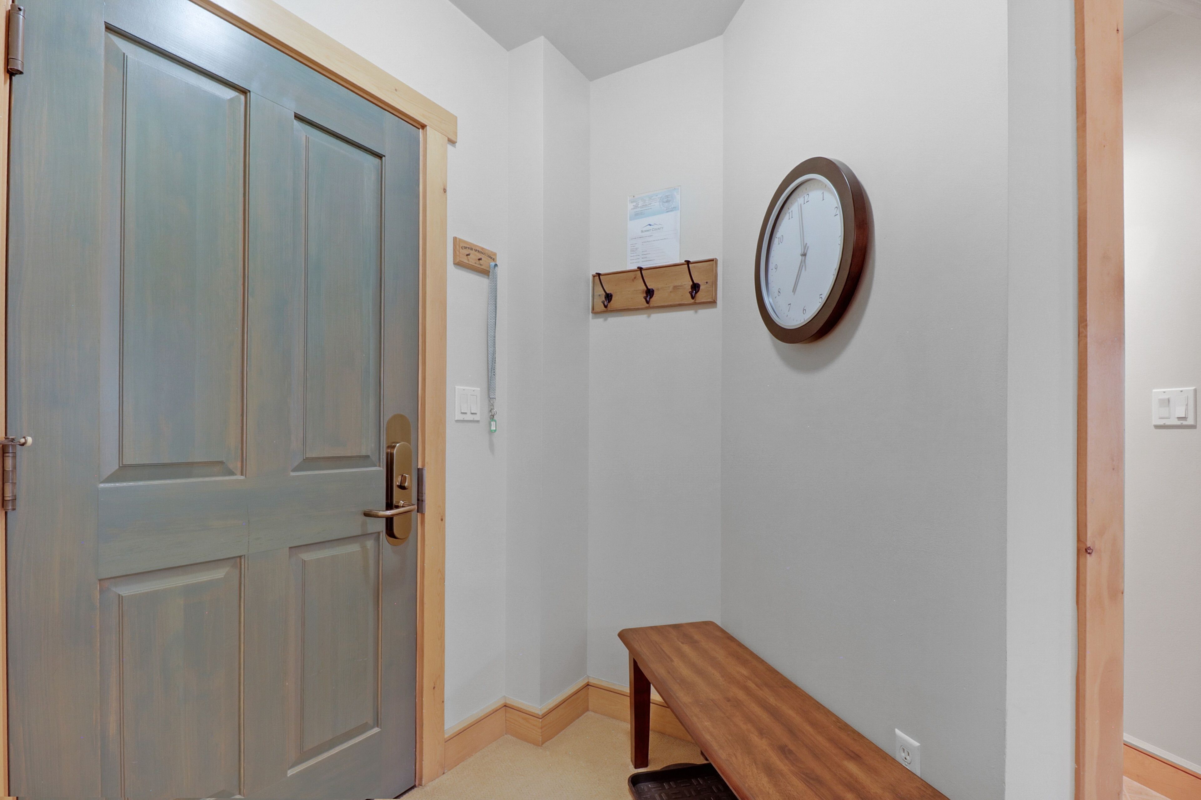 A hallway with a wooden door, a clock, and a bench.