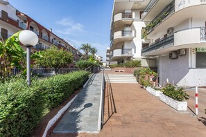 A pathway flanked by neatly trimmed hedges and a row of residential buildings with balconies. - Apartment 'Naxos Sea View' with Sea View, Wi-Fi and Air Conditioning (Naxos)