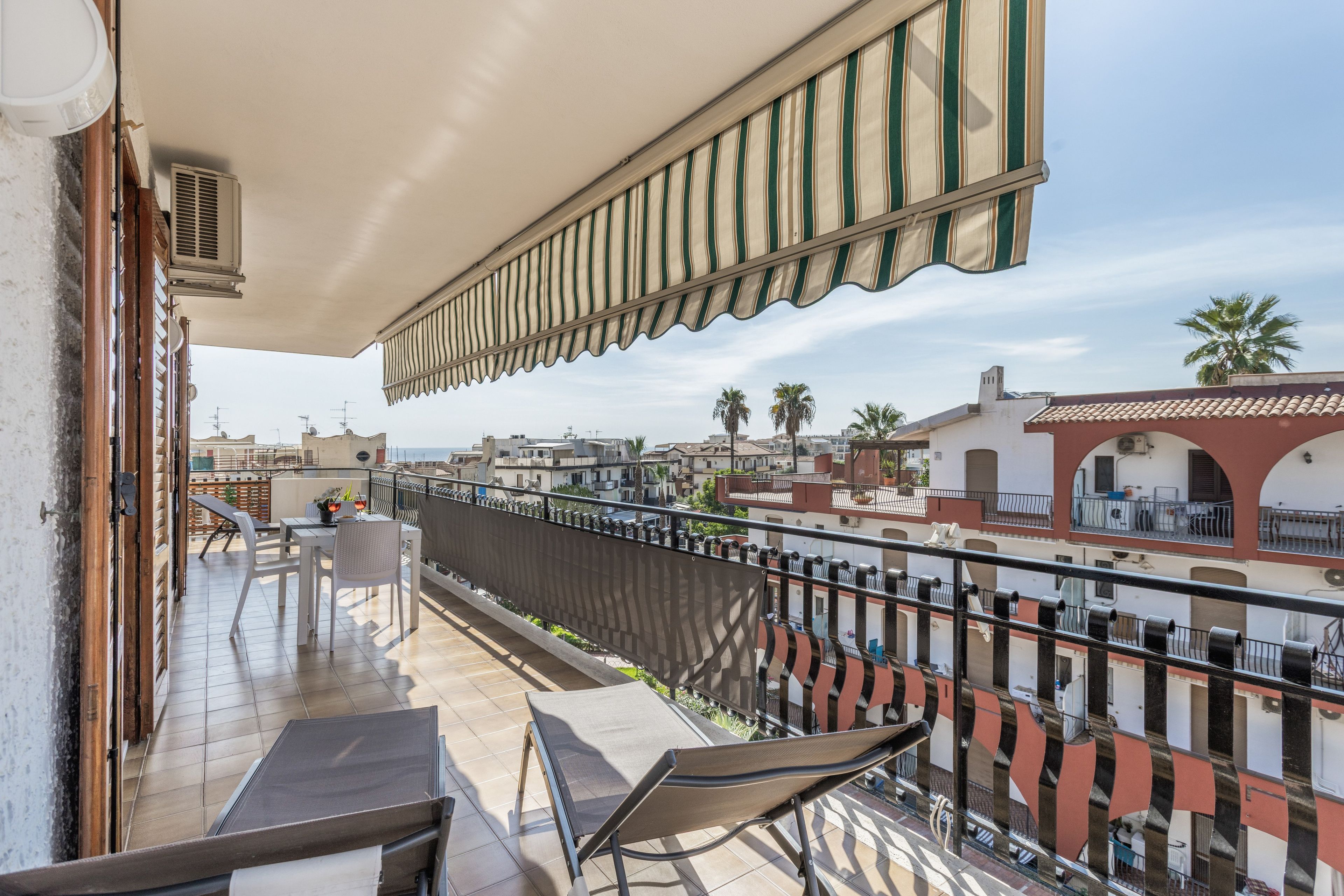 Un balcon avec une table et des chaises, un auvent à rayures et une vue sur le paysage urbain.
