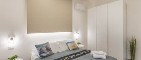 Une chambre d’hôtel avec un lit, une table de chevet agrémentée d’une plante, un climatiseur fixé au mur et une grande armoire.