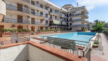 A multi-story residential building with a swimming pool, balconies, and a brick pathway.