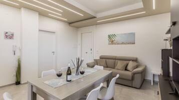 A modern living room with a dining area, featuring a sofa, a coffee table, and a painting on the wall.