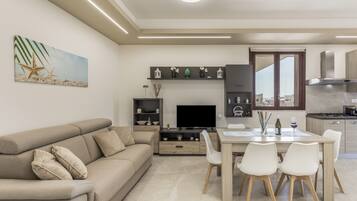 A modern living room with a sofa, TV, and dining area with chairs and a table.