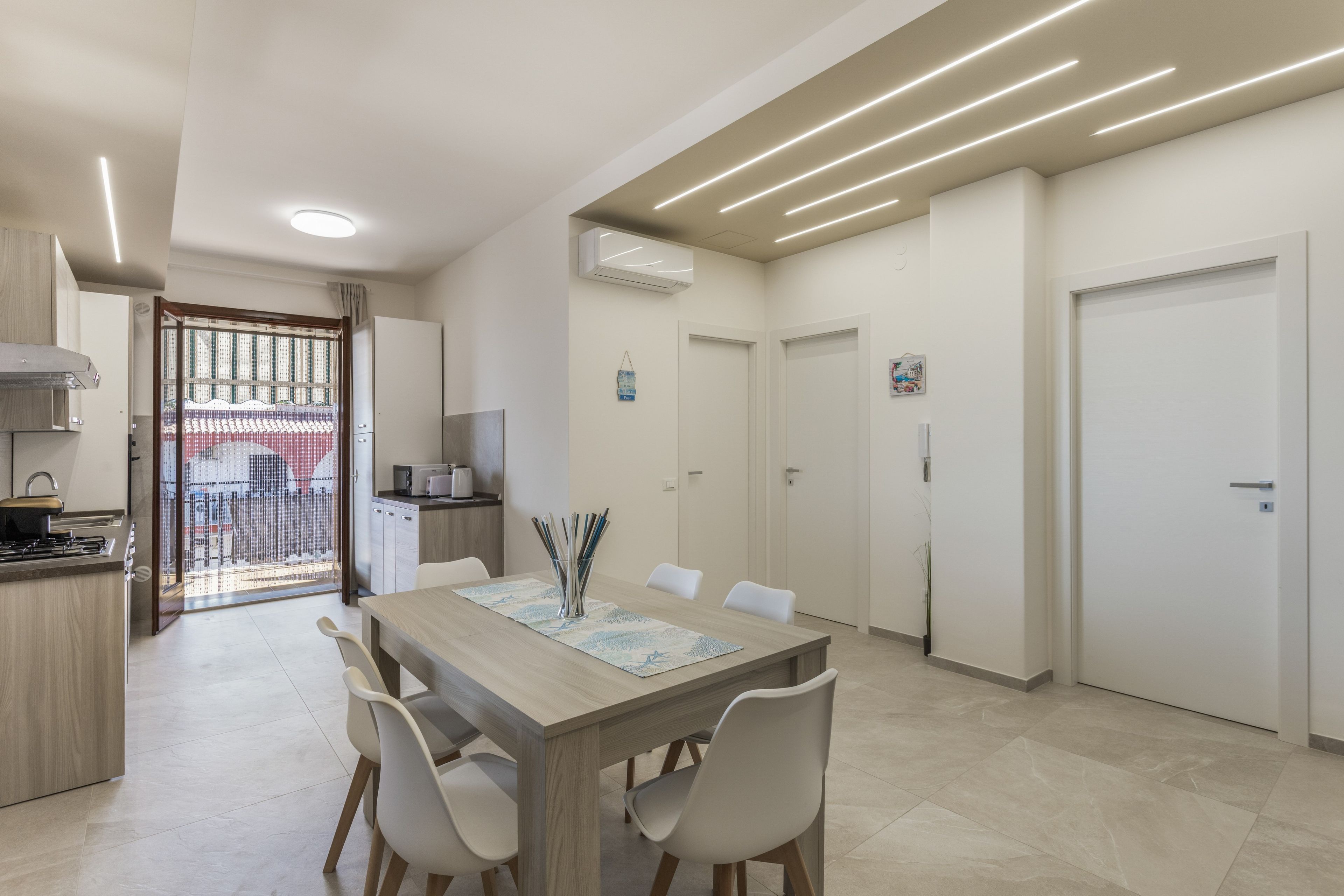 Une cuisine moderne avec un coin repas, comprenant une table en bois, des chaises blanches et une vue à travers une porte vitrée.