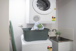 A laundry area with a washing machine, a drying rack, and a sink. - Azure Sea-Renity: Ocean Views, Pool & Gym (Airlie Beach)
