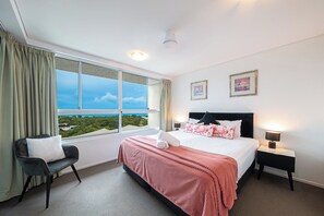 A hotel room with a large window, a bed with a pink blanket, a chair, and a nightstand with a lamp. - Azure Sea-Renity: Ocean Views, Pool & Gym (Airlie Beach)