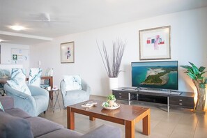 A modern living room with a flat-screen TV, a coffee table, and a sofa. - Azure Sea-Renity: Ocean Views, Pool & Gym (Airlie Beach)