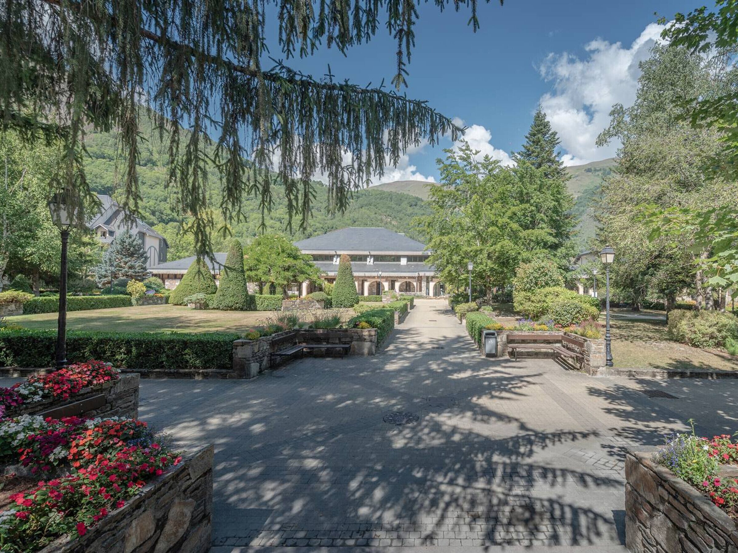 A pathway leading to a building with a symmetrical garden and a mountain in the background.