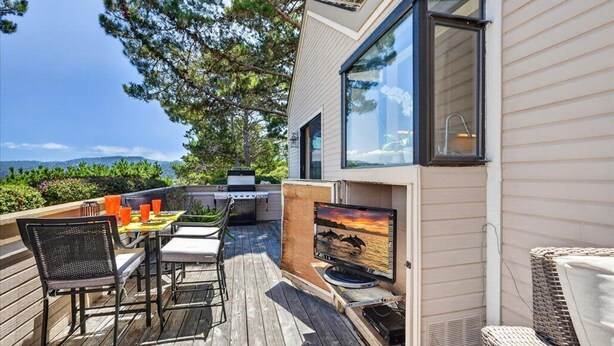 A modern outdoor deck with a dining table, chairs, a grill, and a TV screen displaying a sunset. - 4084 Shibui by the Bay - Skyline Forest Townhouse (Monterey)