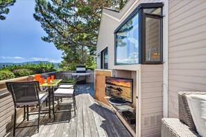 En modern uteplats med ett matbord, stolar, en grill och en tv-skärm som visar en solnedgång.
