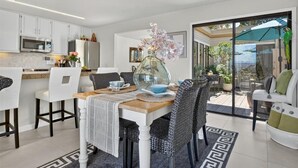 A modern kitchen with white cabinets, a dining area with a glass table, and a view of the outdoors. - 4084 Shibui by the Bay - Skyline Forest Townhouse (Monterey)