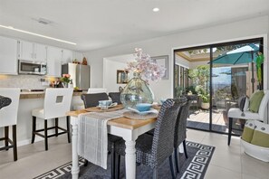 A modern kitchen with white cabinets, a dining area with a glass table, and a view of the outdoors. - 4084 Shibui by the Bay - Skyline Forest Townhouse (Monterey)