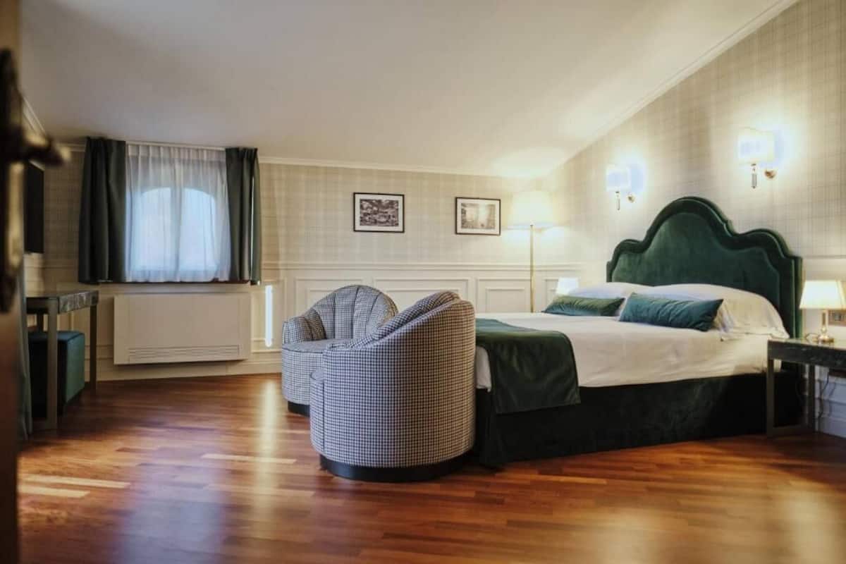 Habitació d'hotel amb llit, cadira, radiador, finestra amb cortines i llums penjades a la paret.