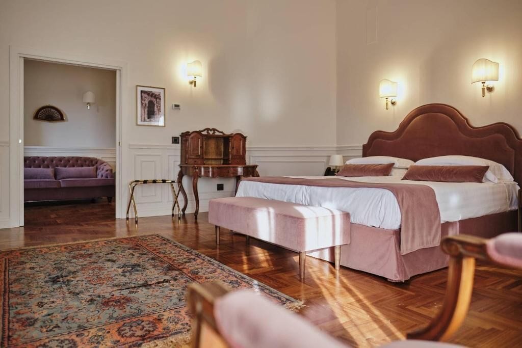 Un dormitorio con una cama doble, un banco, una mesita pequeña, un sofá y una alfombra estampada.