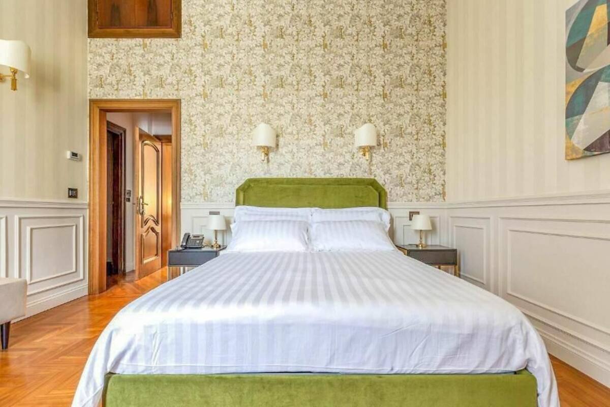 Habitació d'hotel amb un llit gran, dues làmpades de nit, un paper pintat amb flors i una porta de fusta.