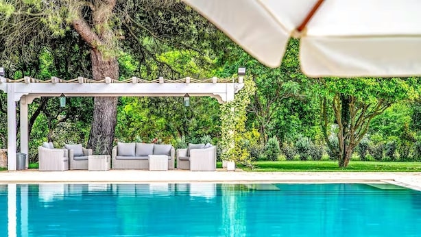 A pool with a pergola and seating area, surrounded by lush greenery. - Villa Lena Puglia (Oria)