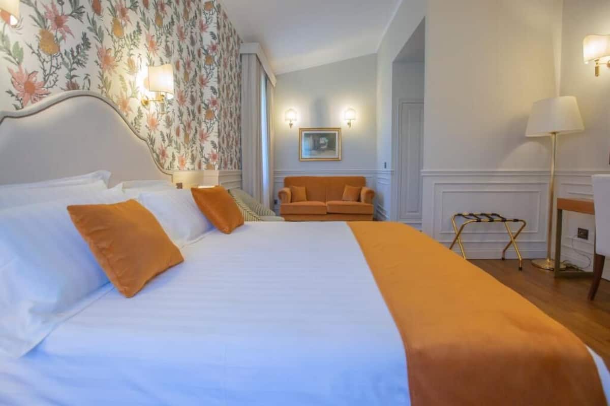 Habitació d'hotel amb un llit gran, un sofà, un escriptori i una làmpada.