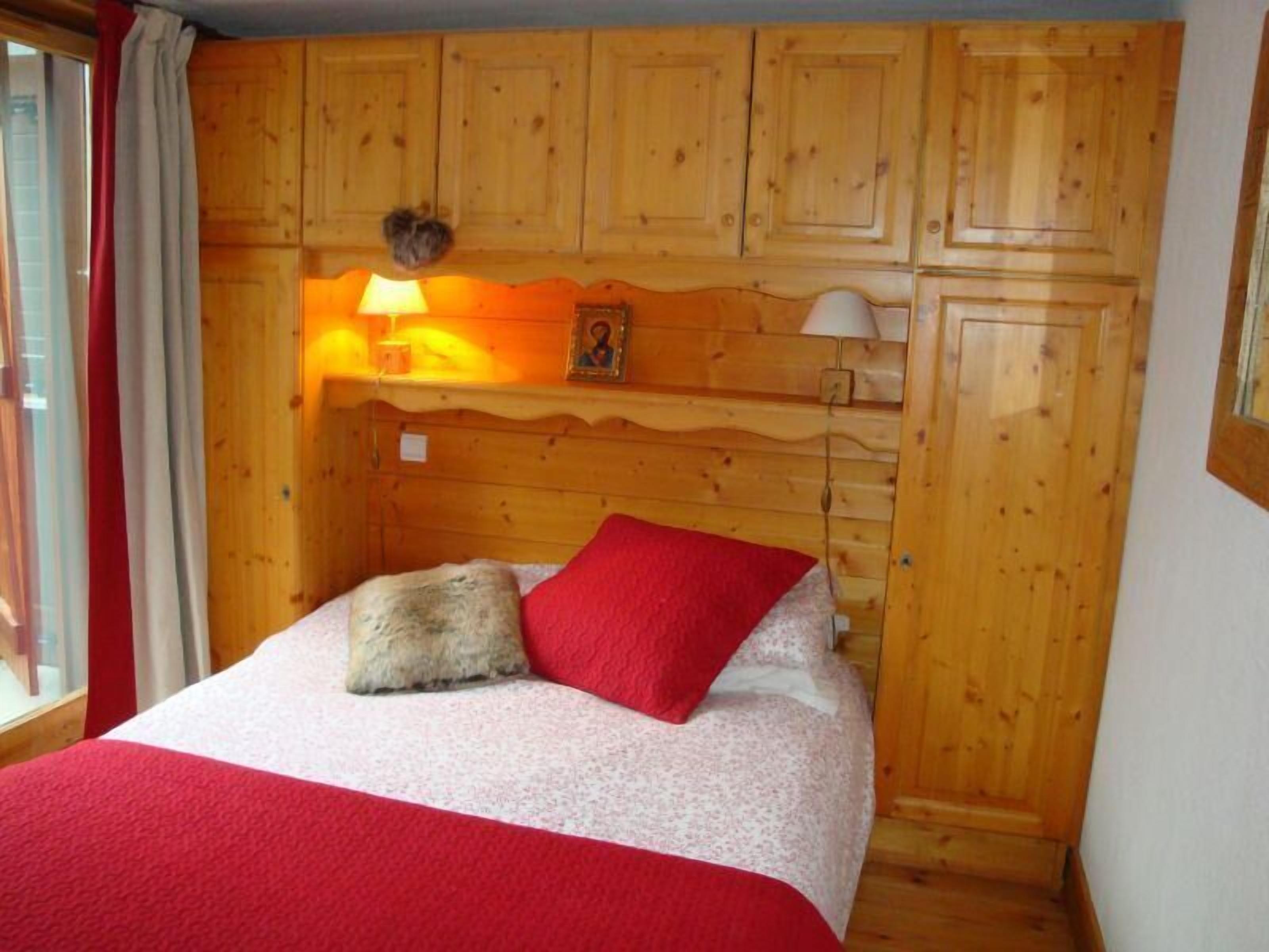 Una habitación tipo cabaña de madera con una cama, un cojín rojo, una lámpara y un marco de fotos en la pared.