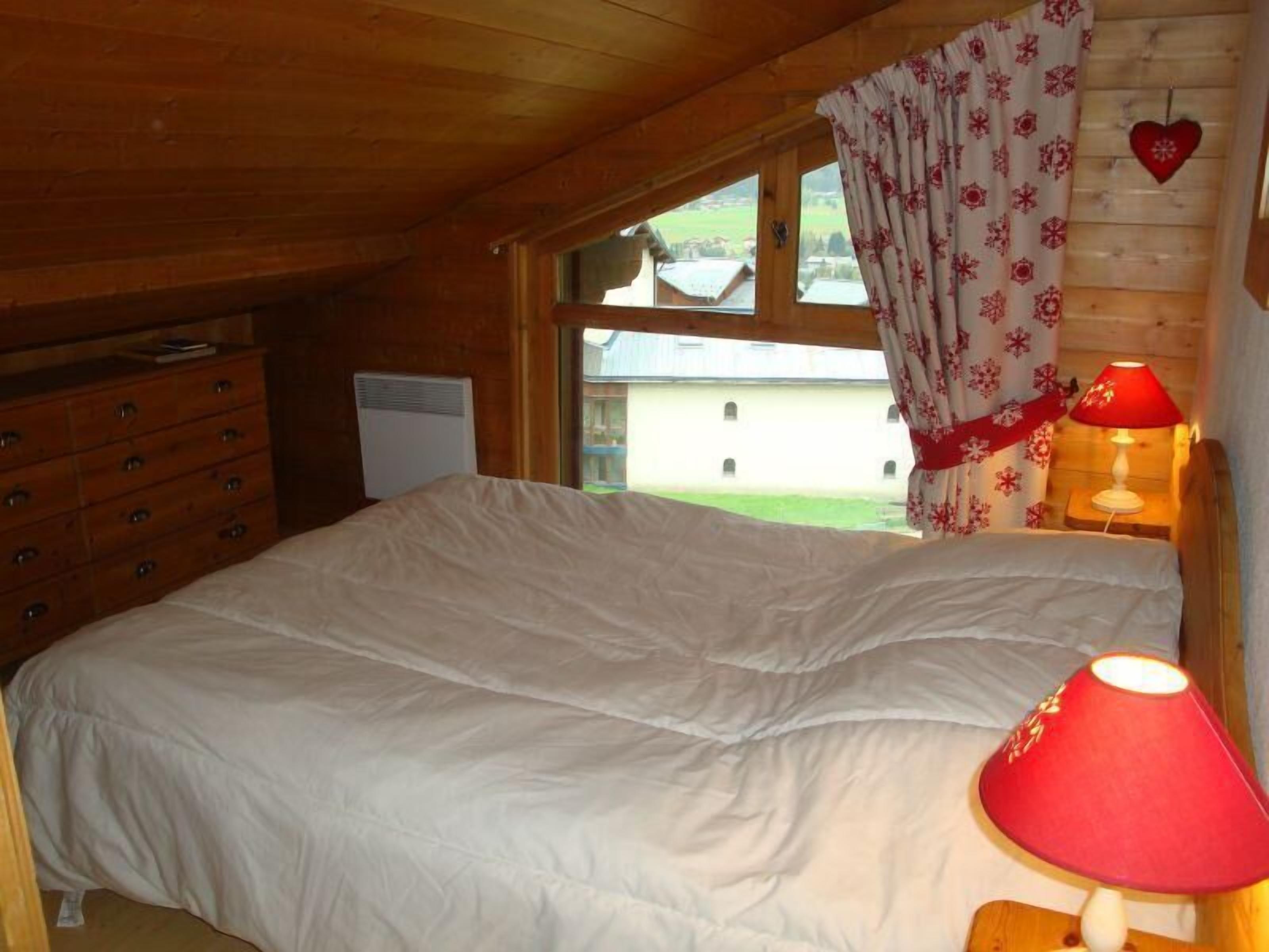 Un dormitorio con cama, cómoda, ventana con cortinas y lámpara.