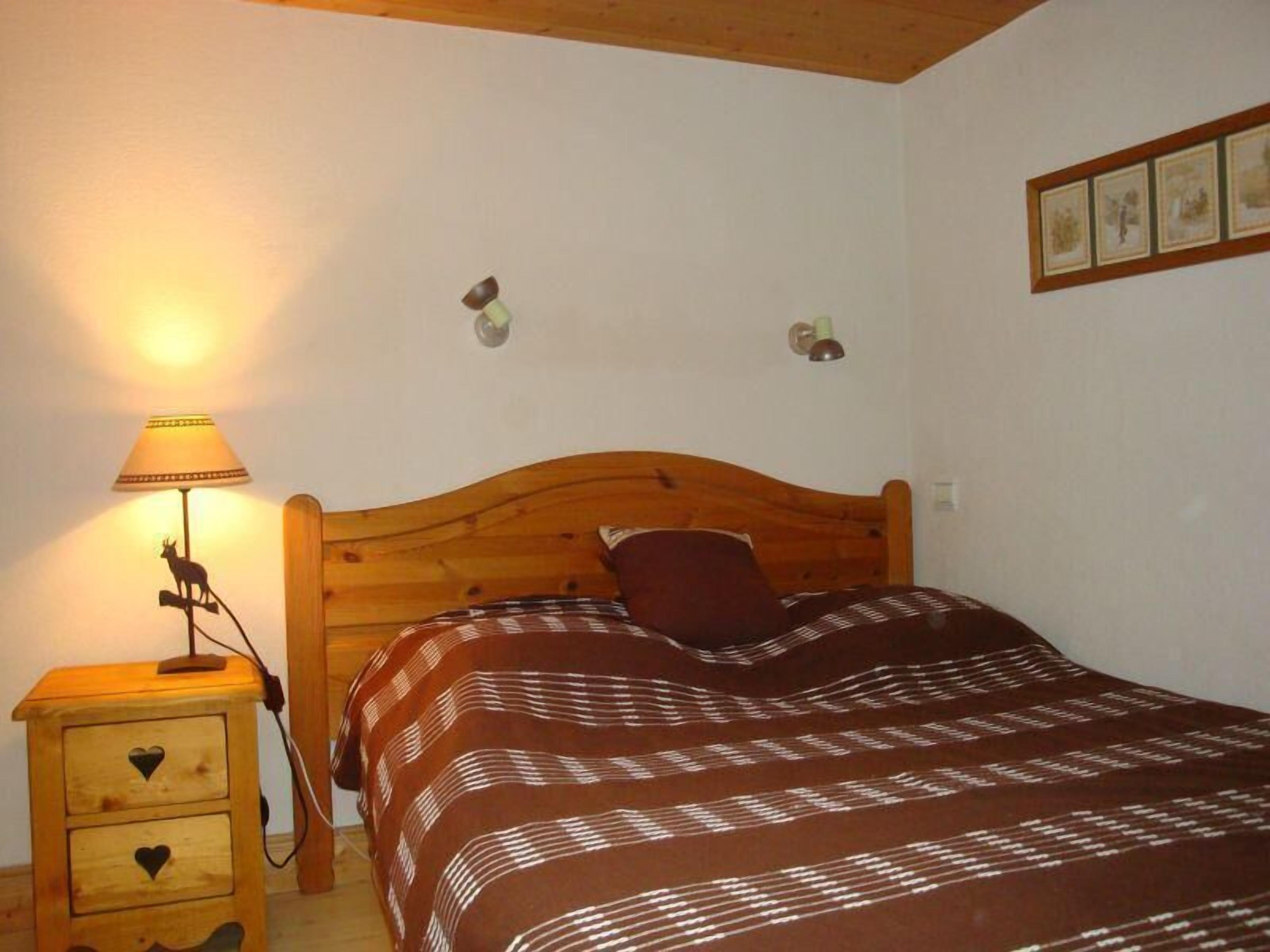 Een slaapkamer met een houten hoofdeinde, een bedlampje, een nachtkastje met lades en een bedovertrek met dessin.