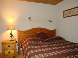 Un dormitorio con cabecera de madera, lámpara de noche, mesita de noche con cajones y colcha estampada.
