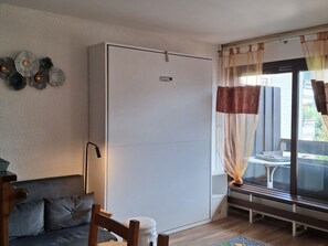 Quarto com sofá, mesa, cadeira, luminária, janela com cortinas e porta deslizante.