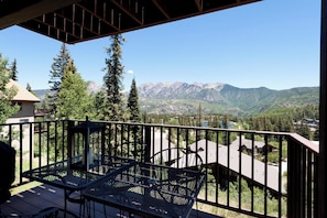 Ein Balkon mit Tisch und Stühlen, der auf eine gebirgige Landschaft mit Bäumen und Gebäuden blickt.