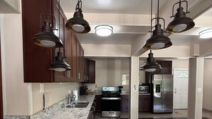 Una cocina amplia con encimeras de granito, electrodomésticos de acero inoxidable e iluminación colgante.