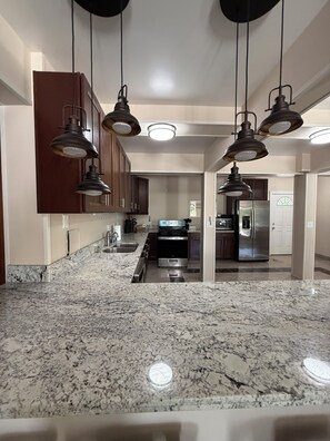 A spacious kitchen with granite countertops, stainless steel appliances, and pendant lighting.