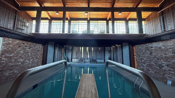 Una piscina interior con vigas de madera, paredes de ladrillo y barandillas de metal.