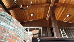 Un interior rústico con vigas de madera a la vista, pared de ladrillo y un amplio ventanal que da a una sala de estar con muebles.
