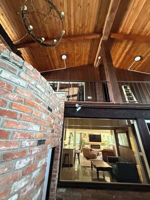 A rustic interior with exposed wooden beams, a brick wall, and a large glass door leading to a living area with furniture.