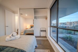 Ein Schlafzimmer mit großem Fenster, einem Bett mit gerolltem Handtuch, einem Nachttisch und Blick ins Freie.