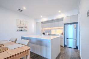 A modern kitchen with white cabinets, a central island, and a built-in refrigerator. - Harbour Haven New Port - Koala Stay Marina Luxe (New Port)