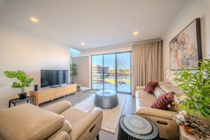 A modern living room with a sofa, a coffee table, a TV, and a large window. - Harbour Haven New Port - Koala Stay Marina Luxe (New Port)