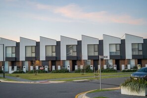 Ein modernes Mehrfamilienhaus mit einheitlicher Fassade, einem Straßenschild mit der Aufschrift 'TORRENS AVE' und einem geparkten Auto davor.