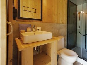 Ein Badezimmer mit Holzwaschtisch, weißem Waschbecken, Toilette und Duschkabine aus Glas.