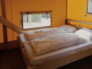 Ein Einzelbett mit weißer Bettwäsche, ein Fenster mit Blick auf Grünflächen und ein Holzboden.